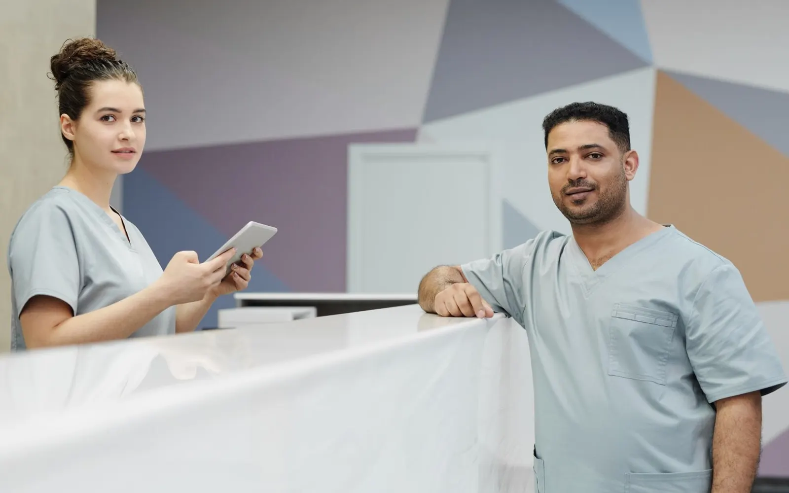Medical receptionist in scrubs greeting a colleague at a clinic front desk