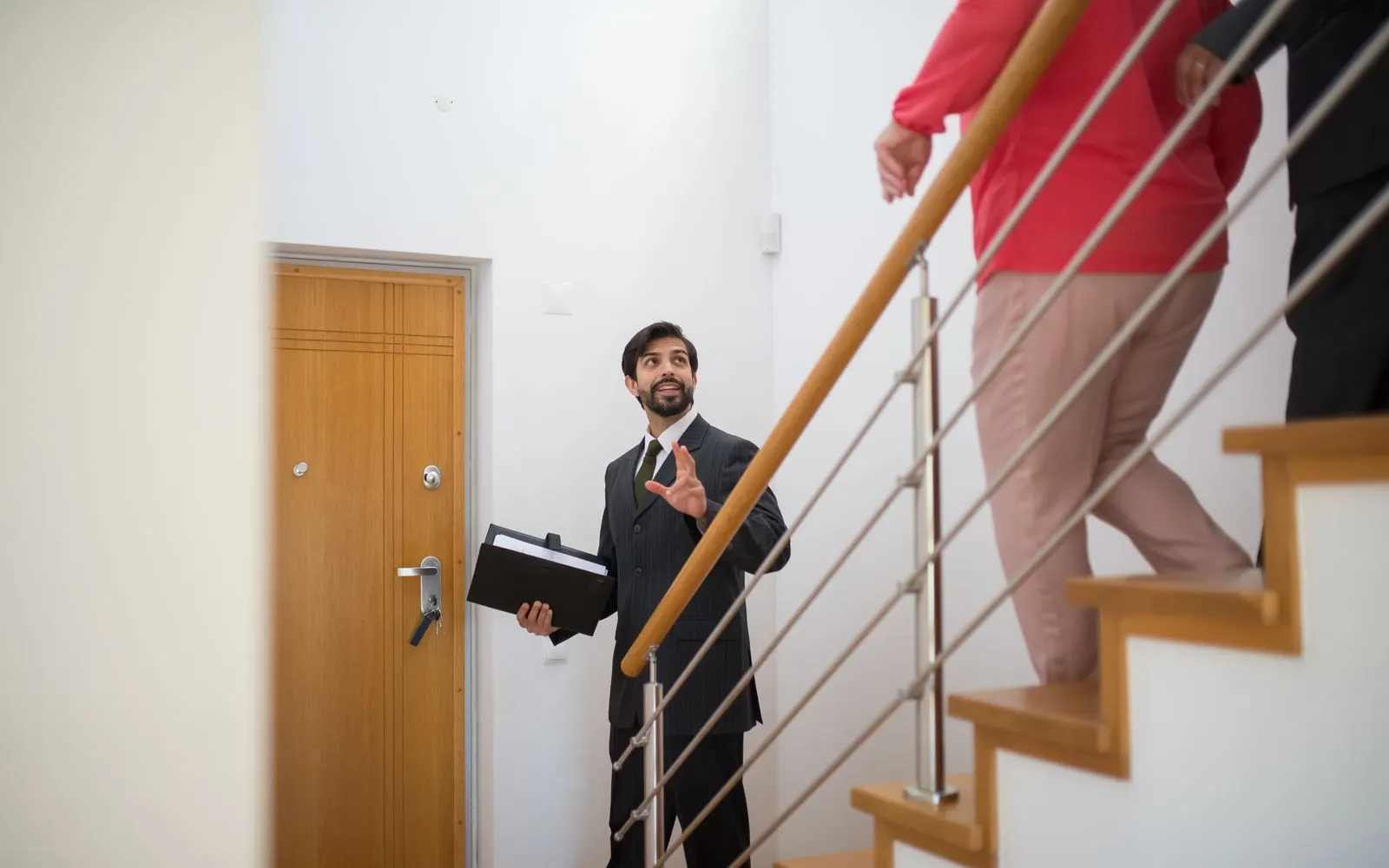 Real estate agent leading a home tour up a staircase while carrying a folder