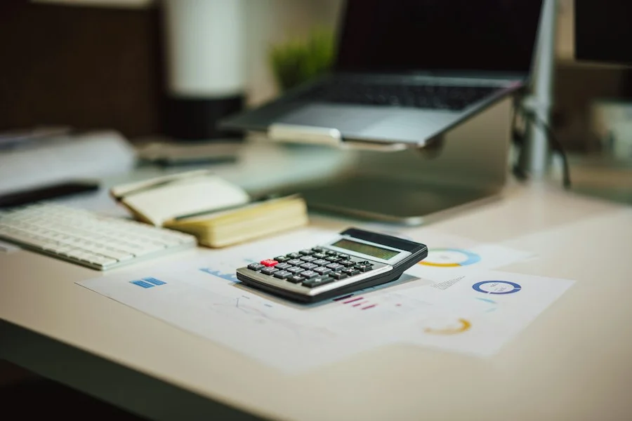 Calculator and charts on a desk next to a laptop