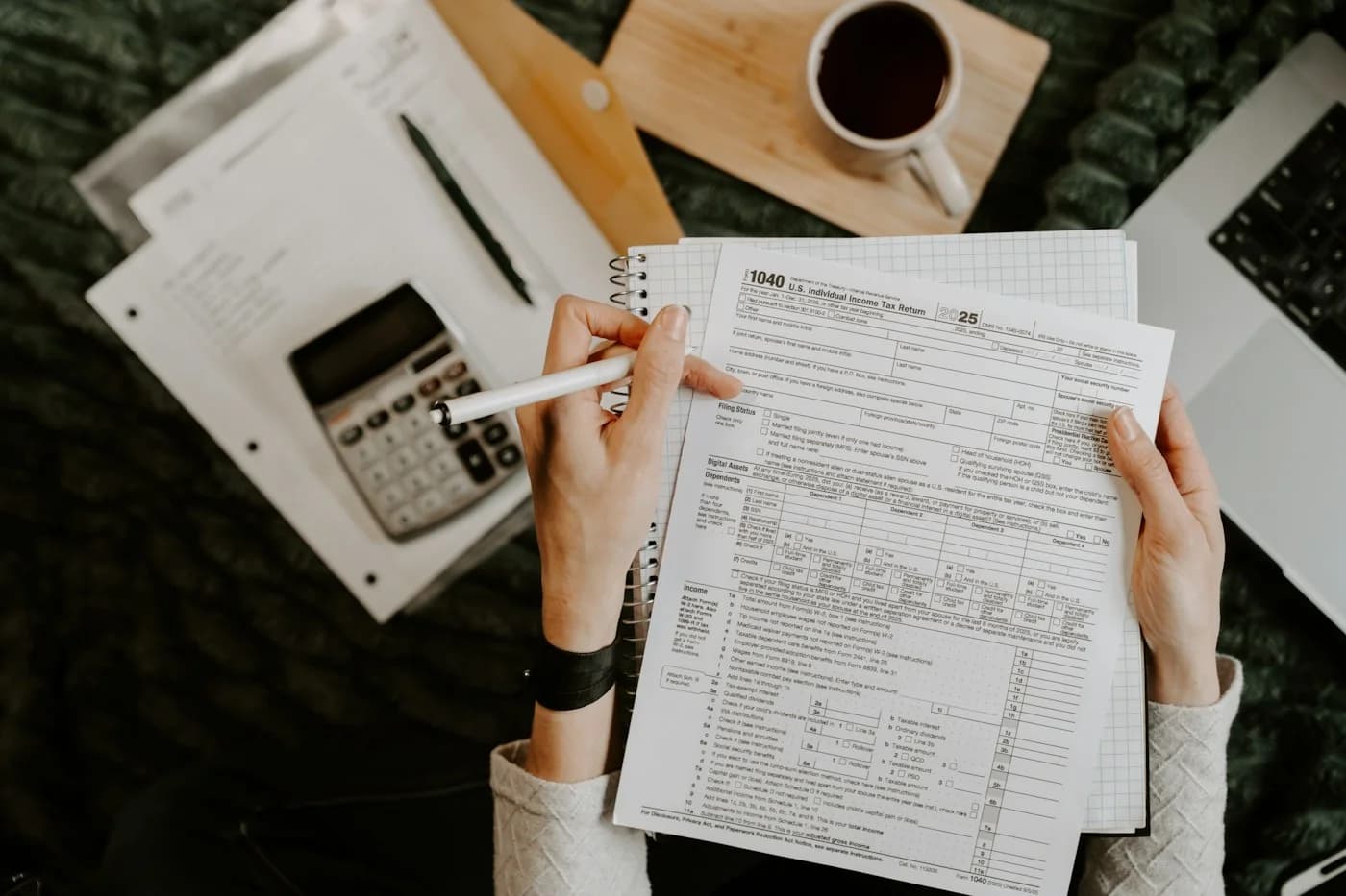 Person filling in a tax form with a calculator, notebook and laptop on the table