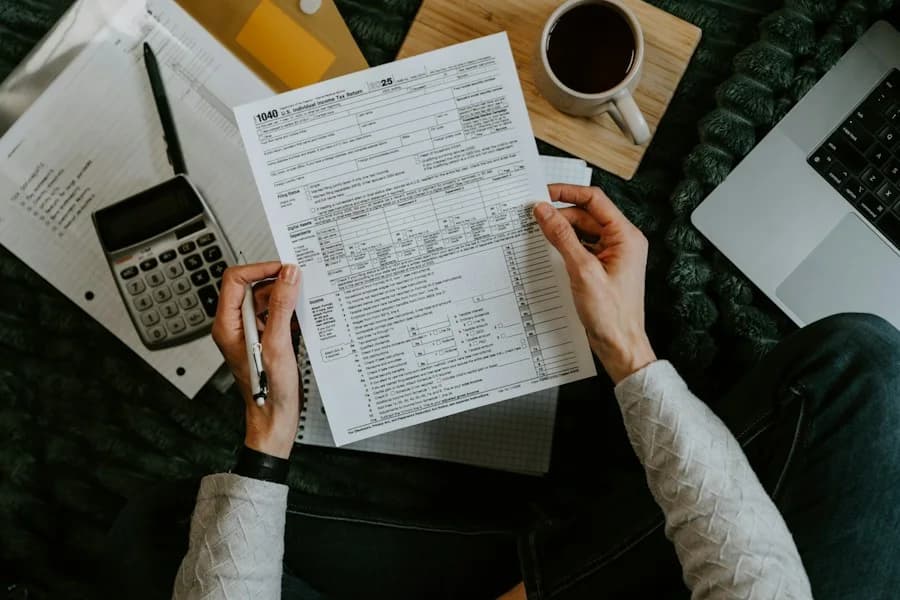 Hands holding a tax form with a calculator and laptop nearby