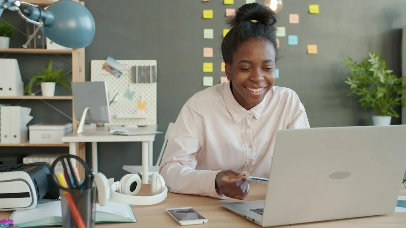 Smiling professional working on a laptop at a desk with sticky notes behind her