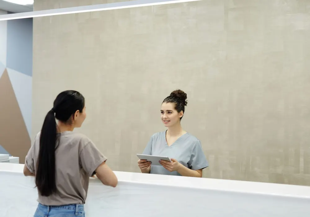 Medical receptionist smiling while assisting a patient at a clinic desk
