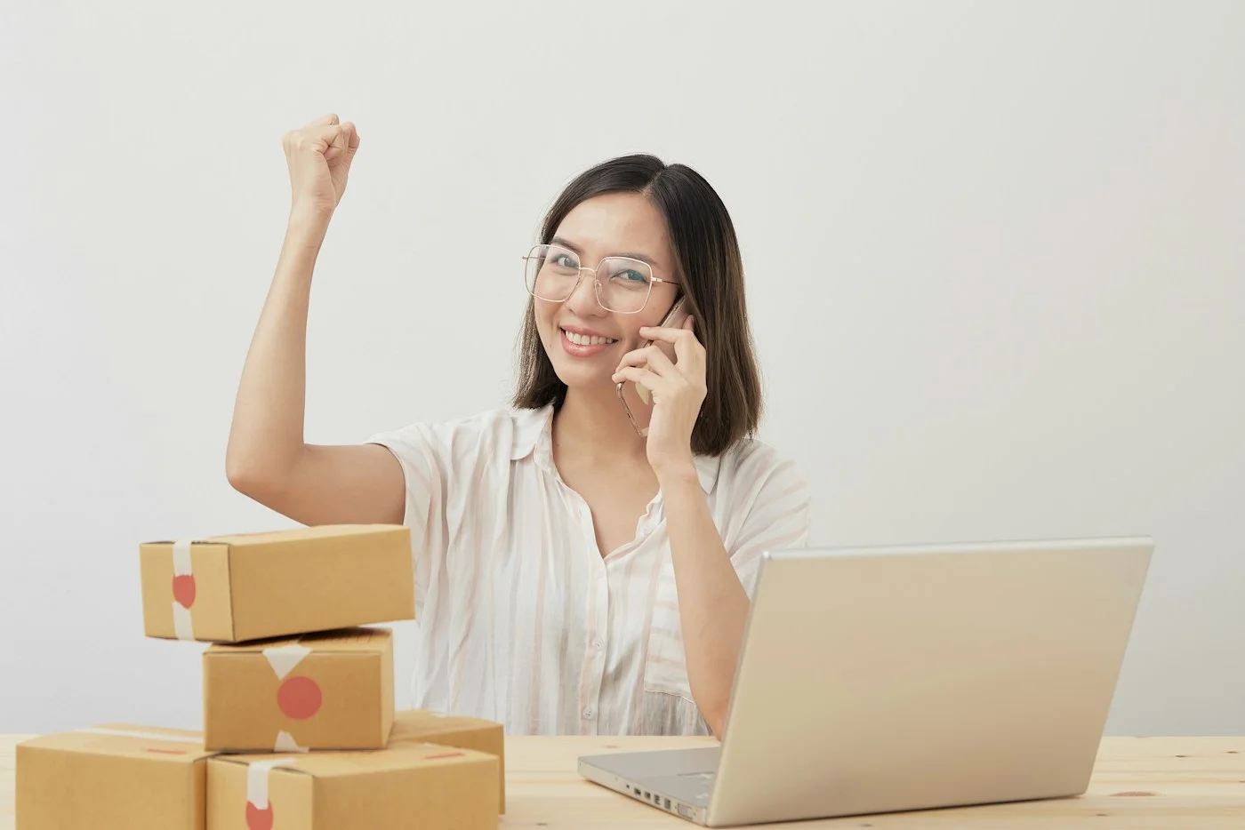 Smiling online shop owner on a phone call at a laptop with parcels stacked beside her