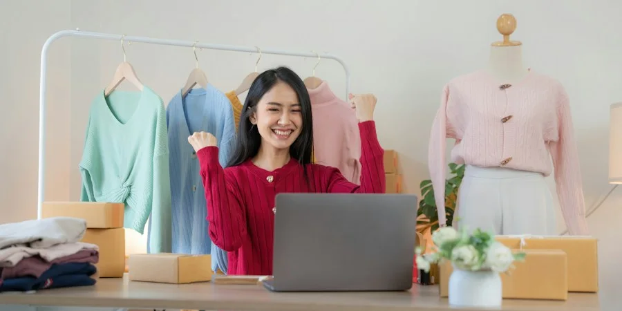 Shop owner celebrating at a laptop in front of a rail of clothes